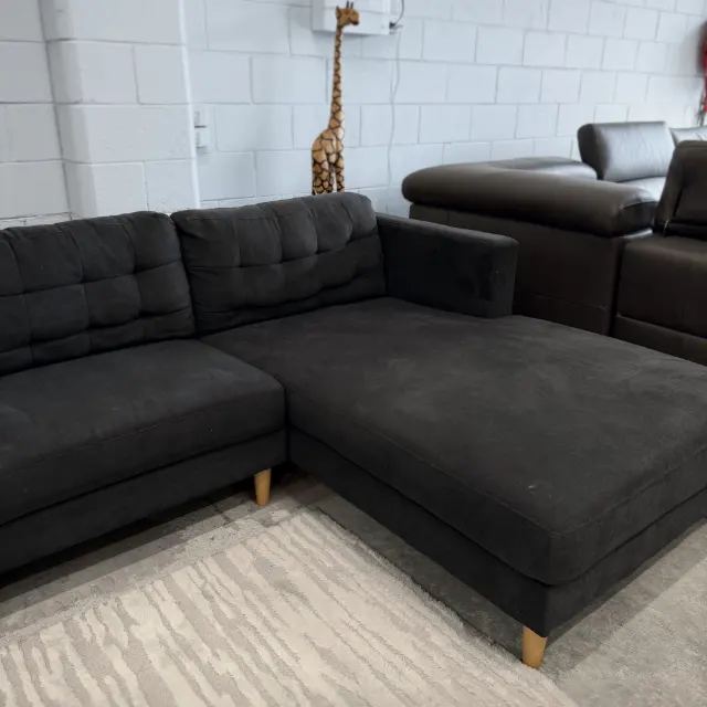 L shape sofa seen from the chaise end, tufted back cushions and timber legs