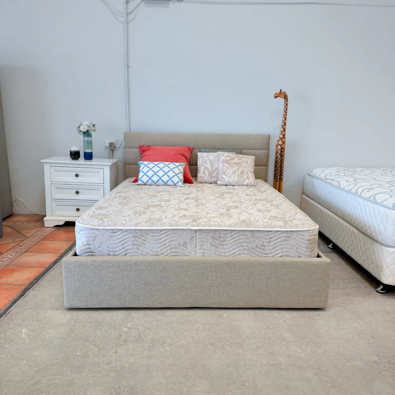 Modern queen storage bed in light grey-beige fabric, shown with a mattress and cushions