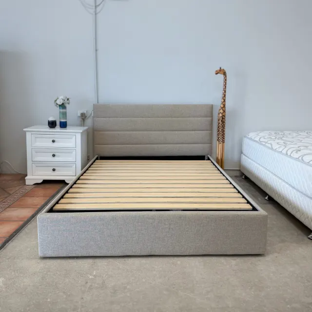 Upholstered queen bed frame from the foot: channel-stitched headboard and timber slat base