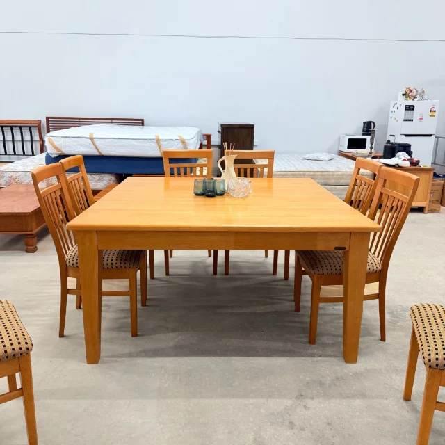 Square timber dining table straight on, with slat-back chairs around it