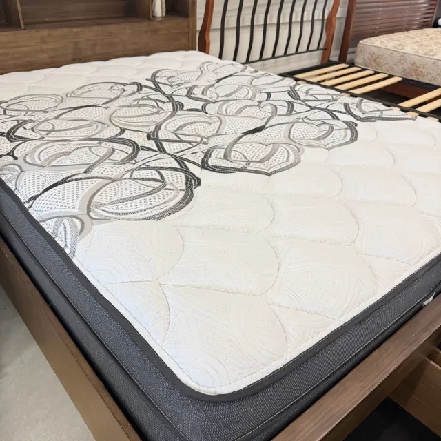 Queen pillow top mattress with a white quilted top and charcoal sides, angled view on a timber bed