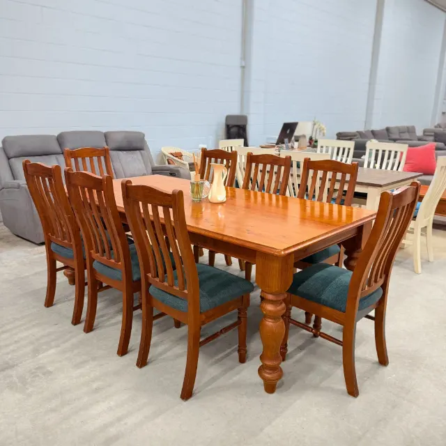 Timber dining table with chunky turned legs and eight chairs with teal padded seats, angled view
